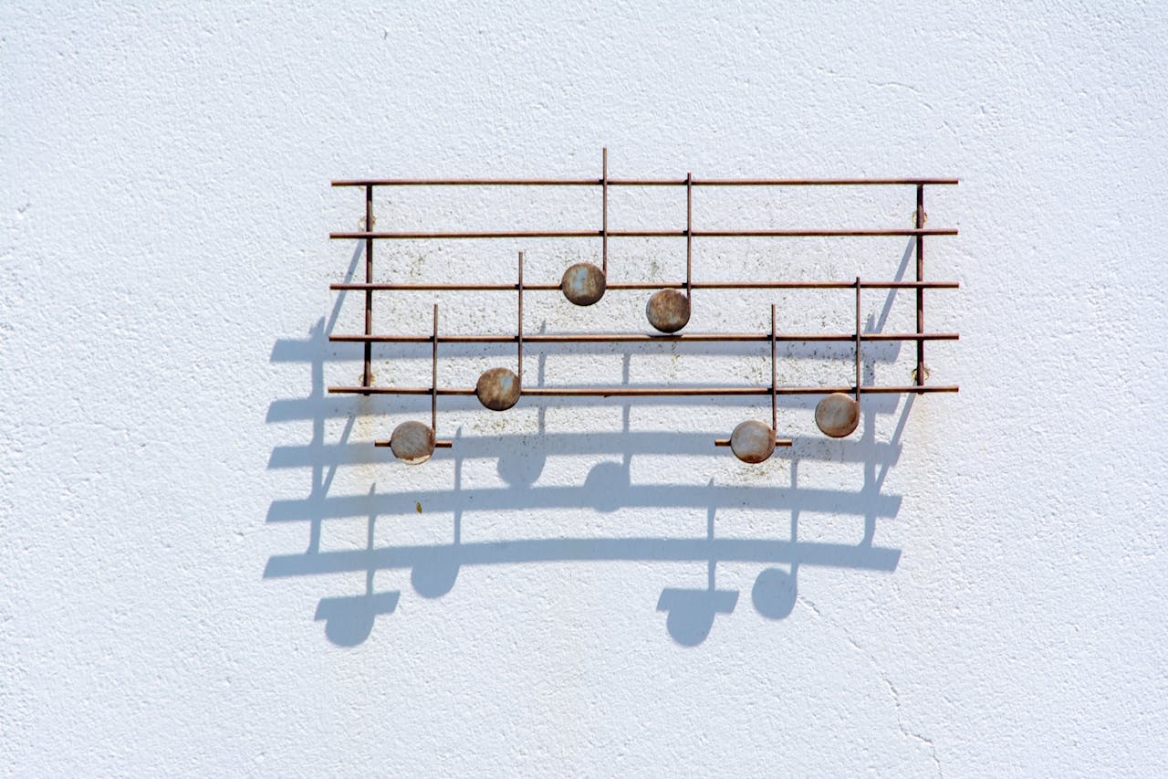 Wall-mounted metal sculpture of musical notes casting shadows on a white surface, creating a minimalist art deco effect.