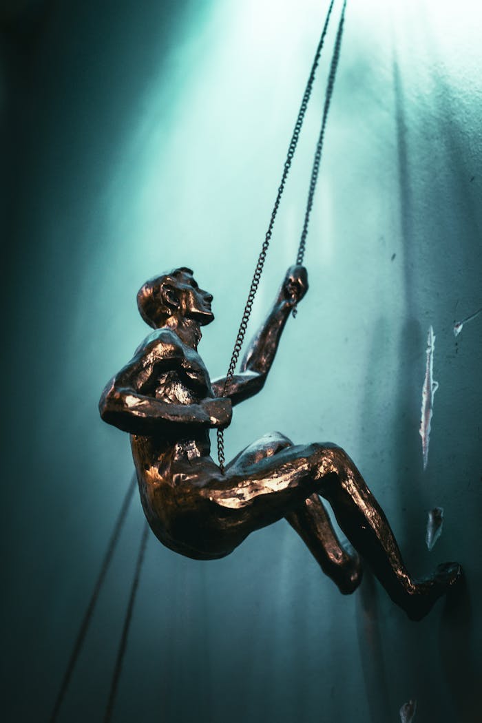 Artistic bronze sculpture of a man climbing using chains, with dramatic lighting.